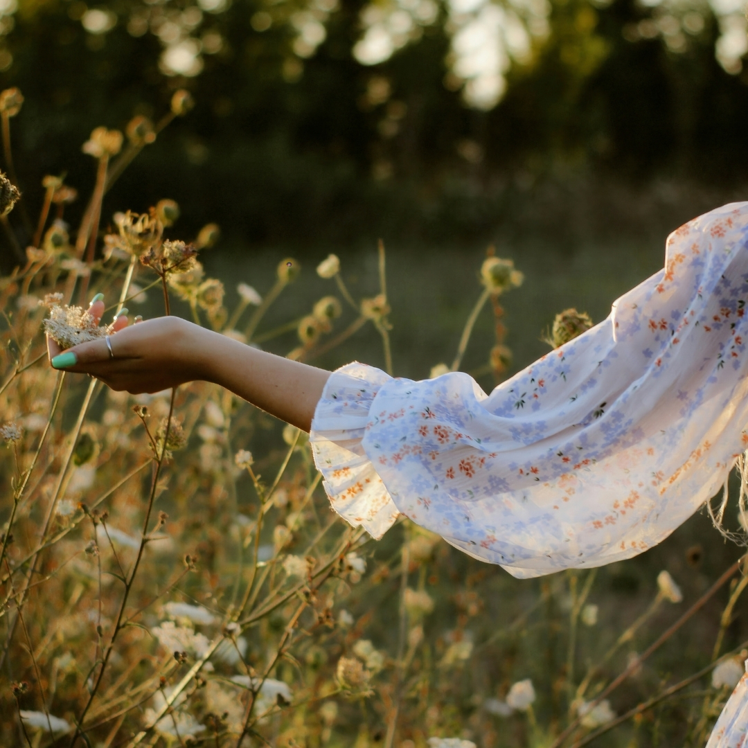 How to be content according to 1 John 2:16, shown by a woman peacefully reaching toward wildflowers as a reminder to find contentment in God rather than worldly desires.